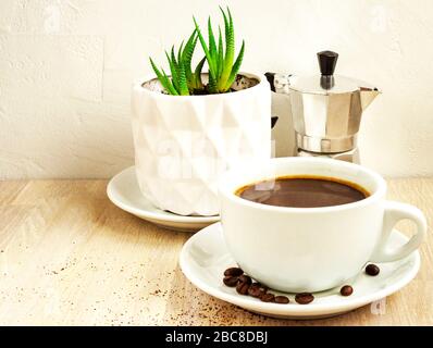 Tasse Kaffee, Untertasse und Bohnen, Aluminiumkaffeemaschine, grüne saftige Pflanze im Topf Stockfoto