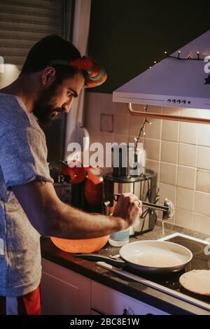 Ernster Mann mit Bart bereitet Pfannkuchen in der Küche am Heiligabend Stockfoto