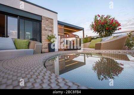 Loungemöbel auf einer modernen Terrasse mit Spiegelung in Glastisch Stockfoto