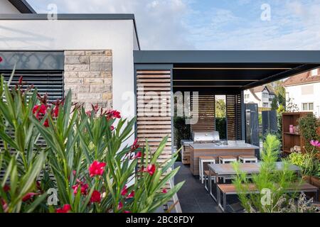 Moderne überdachte Terrasse mit Außenküche, Sitzecke und Kamin mit Orleander und Schmuckkorb Stockfoto