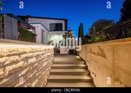 Hauseingang mit Zufahrtsweg und Treppe in der Nacht mit stimmungsvollem Lichtkonzept Stockfoto