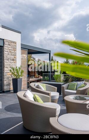 Gartenmöbel aus künstlichem Rattan auf einer großzügigen Terrasse mit einer verschwommenen Palmenfronte im Vordergrund Stockfoto