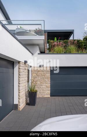 Zwei Garagentore eines exklusiven, modernen Wohnhauses mit einem Auto am Bildrand und einer Terrasse im Hintergrund Stockfoto