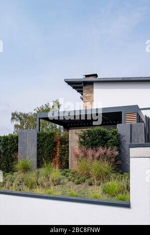 Bepflanzung eines Bettes mit Gräsern vor einem modernen Wohnhaus mit überdachter Terrasse hinter einer Hegerow Stockfoto