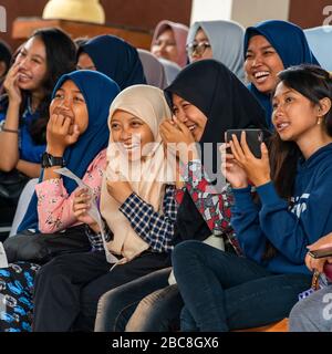 Quadratisches Porträt muslimischer Mädchen, die in einem Publikum in Bali, Indonesien lachen. Stockfoto