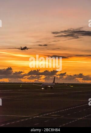 Vertikaler Blick auf Flugzeuge, die bei Sonnenuntergang auf einer Start- und Landebahn starten. Stockfoto