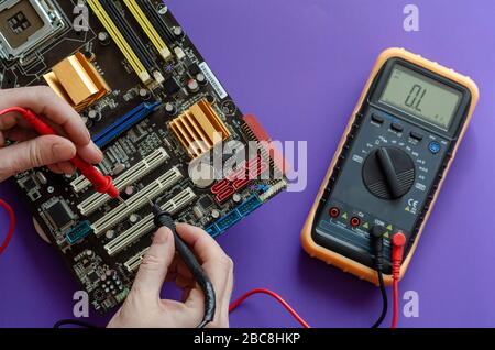 Der Prozess der Reparatur der Hauptplatine. Prüfen des elektrischen Widerstands der Hauptplatine. Die Hände mit einem Digitalmultimeter testen. Ansicht von A Stockfoto