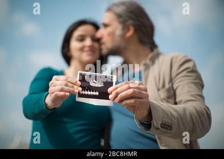 Ein Paar, das Ultraschall im Freien hält und eine Schwangerschaft ankündigt Stockfoto