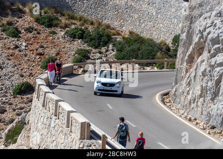 Spanien, Mallorca, Kleinwagen fährt die Bergstraße hinauf zum Leuchtturm Far de Formentor, am Straßenrand laufen zwei Frauen mit einem Kinderwagen und zwei Wanderern Stockfoto