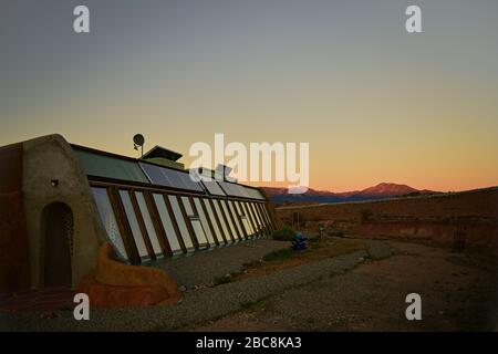 Vorderansicht des selbsttragenden umweltfreundlichen Erdschiffhauses bei Sonnenuntergang mit Bergen im Hintergrund der Landschaft in Toas, New Mexico. Stockfoto