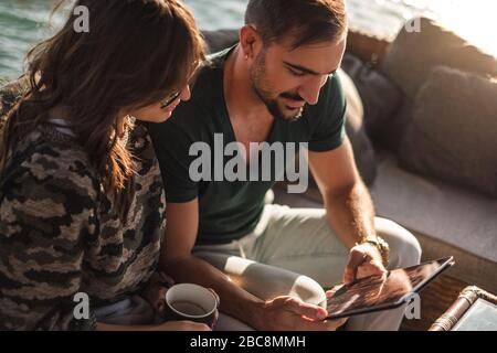 Glückliches Paar lächelt und schaut Tablet-Bildschirm am Fluss an einem sonnigen Tag Stockfoto