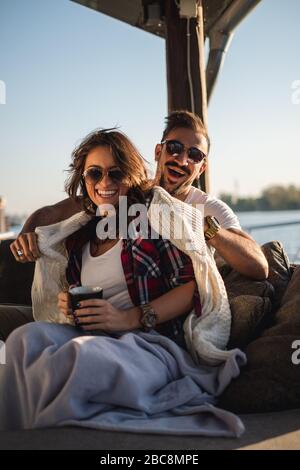 Fröhliches Paar lachend, während Kaffee am Fluss an einem sonnigen Tag trinken Stockfoto
