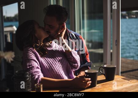 Ein Paar küsst und trinkt Kaffee in einem Haus am Fluss. Schöner sonniger Tag Stockfoto
