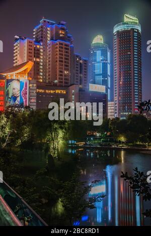 Shanghai, Xuhui, China - 3. Mai 2010: Nachtporträt. Farbenfroh beleuchtete Wolkenkratzer ragen über dunkle Bäume im Xujiahui Park. Stockfoto