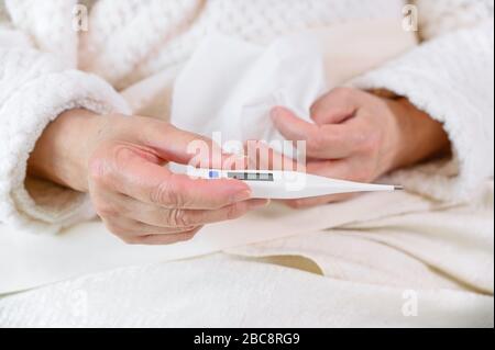 Coronavirus. Kranke ältere Frau, die Gewebe und Thermometer im Bett hält, verärgerte alte reife Frau erwischte Kälte bekam alleine zu Hause Symptome der Grippeimpfung durch Coronavirus. Stockfoto