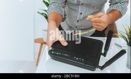 Hand- und lan-Netzwerkkabel mit Mitarbeitern arbeiten am Wireless-Router, Mann arbeitet von zu Hause aus, während er sich während der Covid-19-Gesundheitskrise in Quarantäne befindet Stockfoto