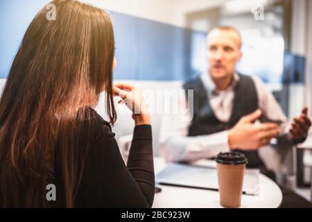 Rückblick auf Geschäftsfrau und Geschäftsmann, die während einer Kaffeepause in einem gemütlichen Kaffeepunkt in einem modernen Büro ein Gespräch führen, selektive Fokussierung auf Th Stockfoto