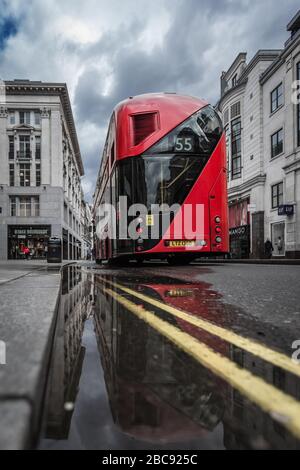 Ein Londoner Bus reflektiert in einer Pfütze an einer menschenleeren Oxford Street im Zentrum Londons während der Krise der pandemischen Gesundheit von Coronavirus in Großbritannien. Stockfoto