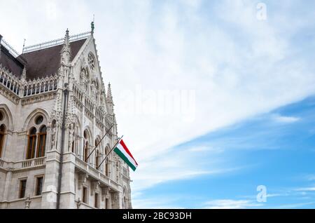 Gebäude des ungarischen Parlaments Orszaghaz in Budapest, Ungarn. Sitz der Nationalversammlung. Haus im neogotischen Stil erbaut. Schwenkende Flagge Ungarns auf dem Haus. Ungarisches Konzept. Stockfoto