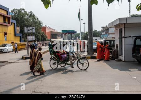 Eine Gruppe von Menschen außerhalb Neu-Delhi Bahnhof, zu Fuß zum und vom Terminal, an einem heißen Tag, mit einer Rikscha im Vordergrund. Stockfoto