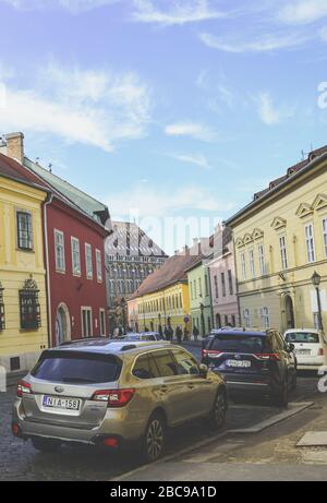 Budapest, Ungarn - 6. November 2019: Schöne historische Straße mit bunten Häusern im historischen Zentrum. Geparkte Autos auf der gepflasterten Straße. Altstadt der ungarischen Hauptstadt. Vertikales Foto. Stockfoto