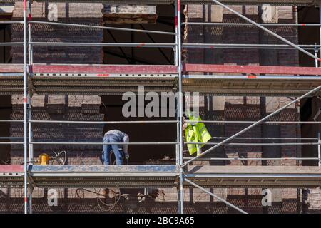 Vorderansicht der Gerüste vor dem alten historischen Gebäude mit schönen Ziegel dekorative Fassade und Fenster auf der renovierten Baustelle. Stockfoto
