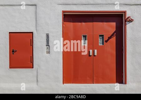 Vorderansicht von außen rot lackiert vintage Stahl Doppeltür und geschlossenen Luftschacht auf raue weiß lackierte Platte Wand. Stockfoto