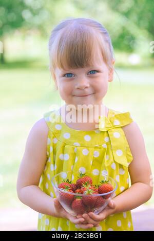 Kleines kleines kleines Mädchen mit einer Glasschale voller köstlicher, frisch gepflückter roter Erdbeeren - Beeren, die im heimischen Garten gesammelt wurden Stockfoto