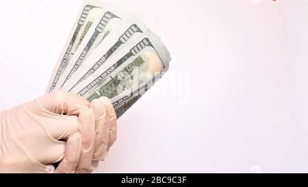 Hände in medizinischen Handschuhen halten ein Bündel Dollar Nahaufnahme auf einem weißen Hintergrund. Das Konzept der Infektion auf Geld, schmutzige Geld-Epidemie coronaviru Stockfoto