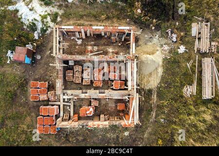 Luftbild der Baustelle für zukünftiges Ziegelhaus, Betonfundament und Stapel gelber Lehmziegel für den Bau. Stockfoto