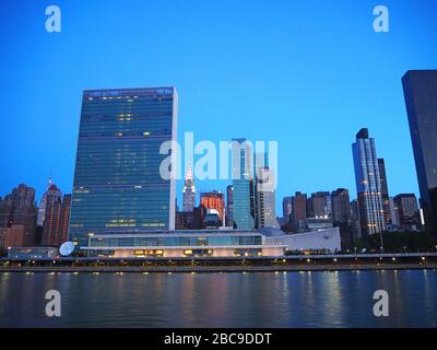 Gebäude des Hauptquartiers der Vereinten Nationen mit Chrysler Building im Hintergrund im Morgengrauen, vom East River, New York, USA aus gesehen Stockfoto