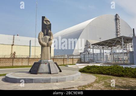 PRIPYAT, UKRAINE - 25. April 2019: Denkmal für die Liquidatoren von Tschernobyl und vierter Reaktor ohne umschließenden Sarkophag. Kernenergieplan Von Tschornobyl Stockfoto