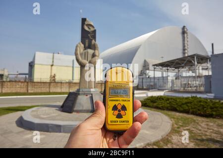 PRIPYAT, UKRAINE - 25. April 2019: Denkmal für die Liquidatoren von Tschernobyl und vierter Reaktor ohne umschließenden Sarkophag. Kernenergieplan Von Tschornobyl Stockfoto