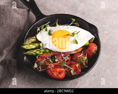 Gebratenes Ei auf Toast mit geröstetem Tomatenspargelfrühstück, gesundes Essen, Stockfoto