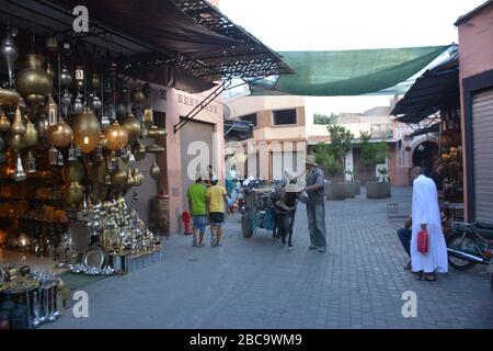 Ein einheimischer alter Mann mit Esel und Wagen geht durch eine teilweise überdachte Straße mit einem traditionellen marokkanischen Lampenladen in Marrakesch Medina, Marokko Stockfoto