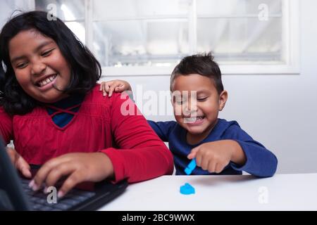 Junge Geschwister sitzen zu Hause vor einem Laptop während des Fernunterrichts-Klassenzimmers zusammen. Stockfoto