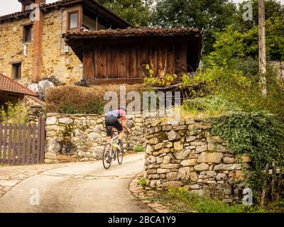 Straßenradsport in Asturien, Nordspanien. Rennradrennfahrer erklimmen die steile Dorfstraße von Llanuces, Cordillera Cantabrica, Principado de Asturias, S Stockfoto