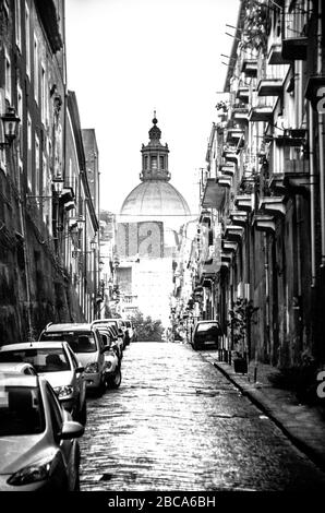 Italienische Straßenszene aus Kopfsteinpflaster in Schwarz und weiß mit der Kuppel einer Kirche am Ende der Straße. Stockfoto