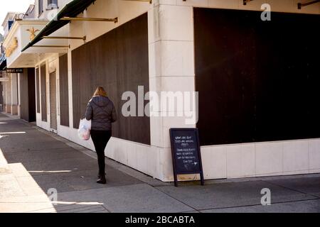 Vancouver, Kanada, 03. April 2020. Eine Frau läuft an Geschäften in der South Granville Street vorbei, die geentert wurden, um während der COVD-19-Pandemie Beutezüge zu verhindern. Stockfoto