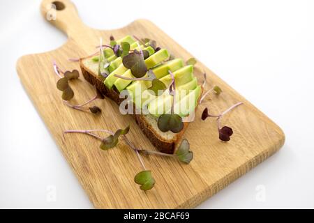 Radie-Mikrogrüns als Garnierung auf geschnittenem Avocado mit glutenfreiem Brot auf einem Holzbrett Stockfoto