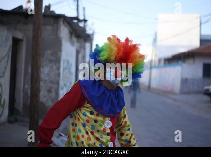 Gaza, Palästina. April 2020. Eine palästinensische Jugend, die als Clown verkleidet war, während sie Schutzhandschuhe und eine Maske trug, inszenierte eine Straßendarbietung, um Kinder zu unterhalten, die aufgrund des Ausbruchs des Corona-Virus in Khan Yunis im südlichen Gazastreifen zu Hause gefangen waren. Credit: SOPA Images Limited/Alamy Live News Stockfoto