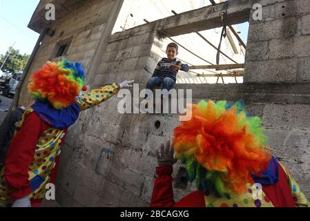 Gaza, Palästina. April 2020. Palästinensische Jugendliche, die als Clowns verkleidet sind und Schutzhandschuhe tragen, sind eine Straßenvorstellung, um Kinder zu unterhalten, die aufgrund des Corona-Virus-Ausbruchs in Khan Yunis, dem südlichen Gazastreifen, zu Hause gefangen sind. Credit: SOPA Images Limited/Alamy Live News Stockfoto