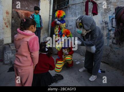 Gaza, Palästina. April 2020. Palästinensische Jugendliche, die als Clowns verkleidet sind und Schutzhandschuhe tragen, sind eine Straßenvorstellung, um Kinder zu unterhalten, die aufgrund des Corona-Virus-Ausbruchs in Khan Yunis, dem südlichen Gazastreifen, zu Hause gefangen sind. Credit: SOPA Images Limited/Alamy Live News Stockfoto