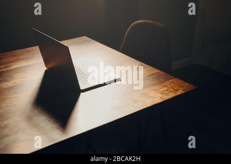 Ein Laptop auf einem Holztisch in einem dunklen Bereich mit Lederstuhl. Draufsicht. Stockfoto