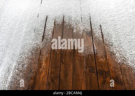 Schnee auf einem Holzboden einer offenen Terrasse im Hintergrund. Stockfoto