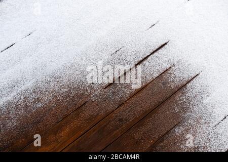 Schnee auf einem Holzboden einer offenen Terrasse im Hintergrund. Stockfoto