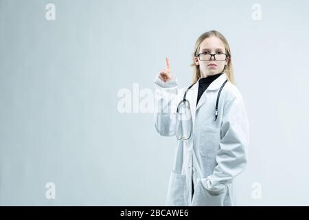 Lustige kleine Mädchen, die eine Brille tragen, die als Arzt oder Krankenschwester in einem weißen Labormantel mit Stethoskop über einem weißen Hintergrund mit Kopierraum gekleidet ist Stockfoto