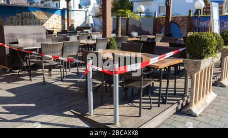 Terrasse eines Restaurants mit Stühlen und Tischen. Mit rotem - weißem Band geschlossen. Geschlossen aufgrund von Einschränkungen im Zusammenhang mit dem Coronavirus (Covid-19). Stockfoto