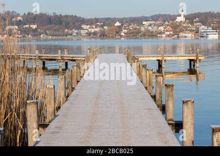 Blick auf einen leeren Steg am Starnberger See. Die Oberfläche des Stegs ist mit Frost bedeckt. Im Hintergrund die Stadt Starnberg. Stockfoto