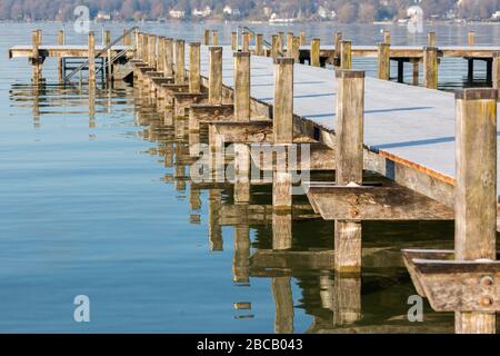 Blick auf die Seite eines mit Frost bedeckten Stegs am Starnberger See (Starnberger See). Mit vielen Holzpfählen und entsprechenden Wasserspiegelungen. Stockfoto